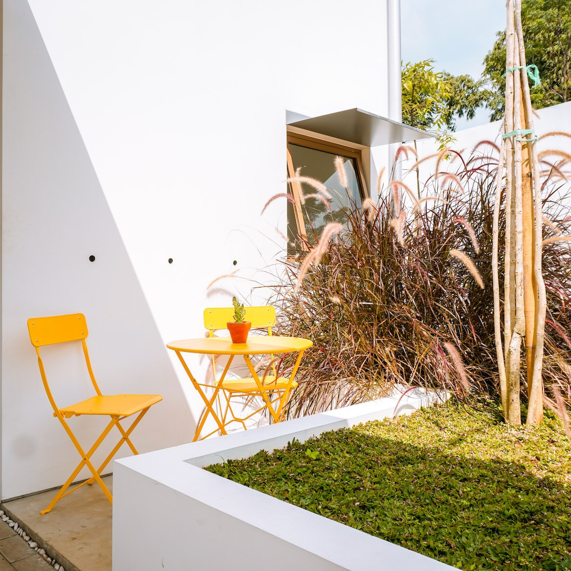 Orange chairs and table on the garden patio, in front of the white exterior of the Eureka House by Luwist Spatial.