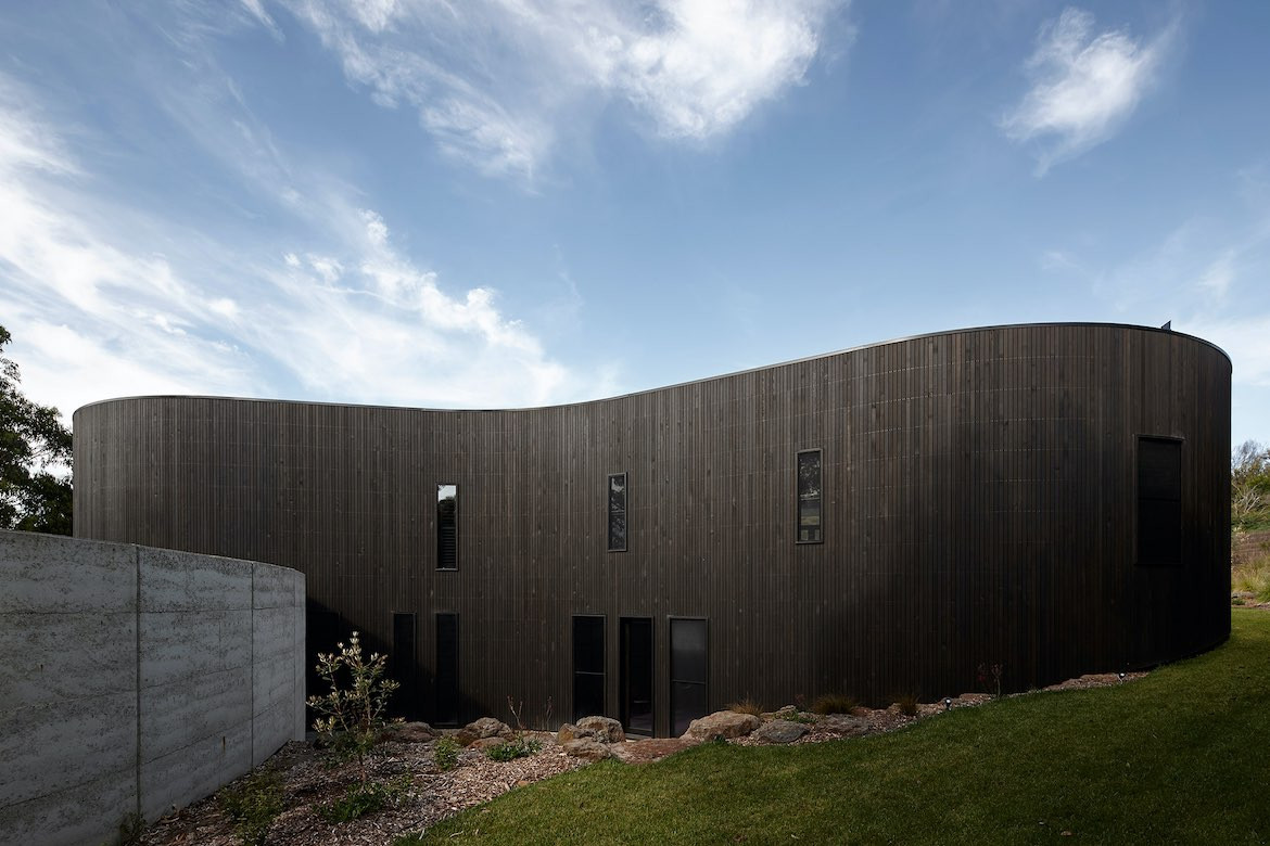 A view of the dark wooden cladding on the side of Portsea house and the subtle slope of the site.