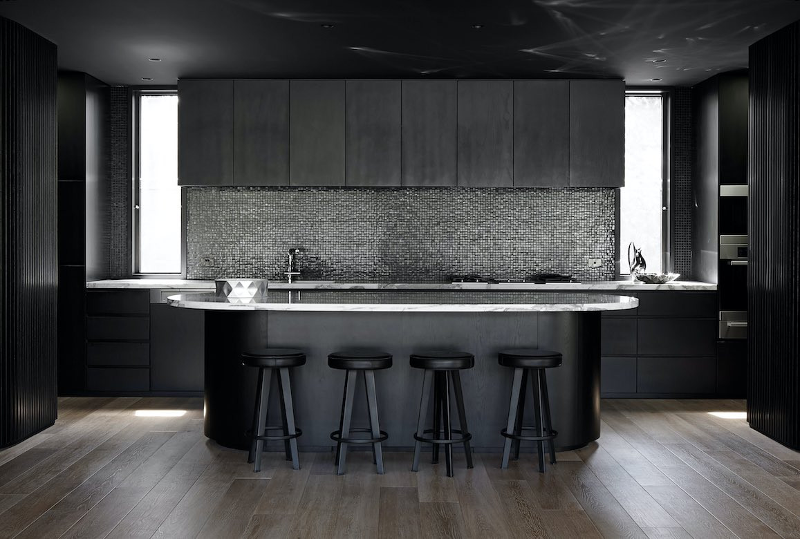 Four black stools line the kitchen island bench with shiny dark mosaic splashback tiling behind in the kitchen of Portsea House