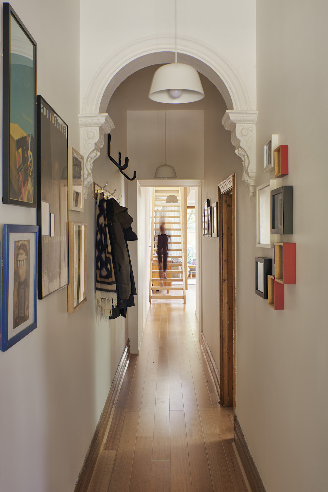 A white entrance hallway has high ceilings and an archway with photographs covering the walls.