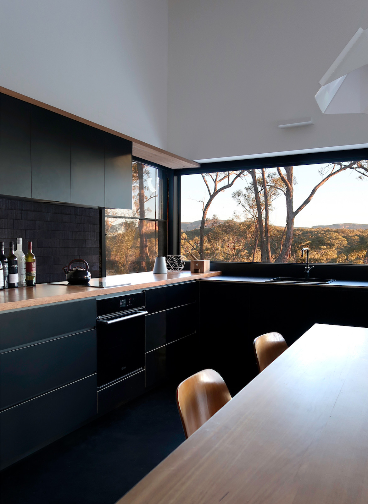 Windows in the dark timber kitchen look out to the bush surrounding the house.