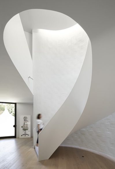 A white staircase spirals upwards in front of a rendered brick wall in Brush House.