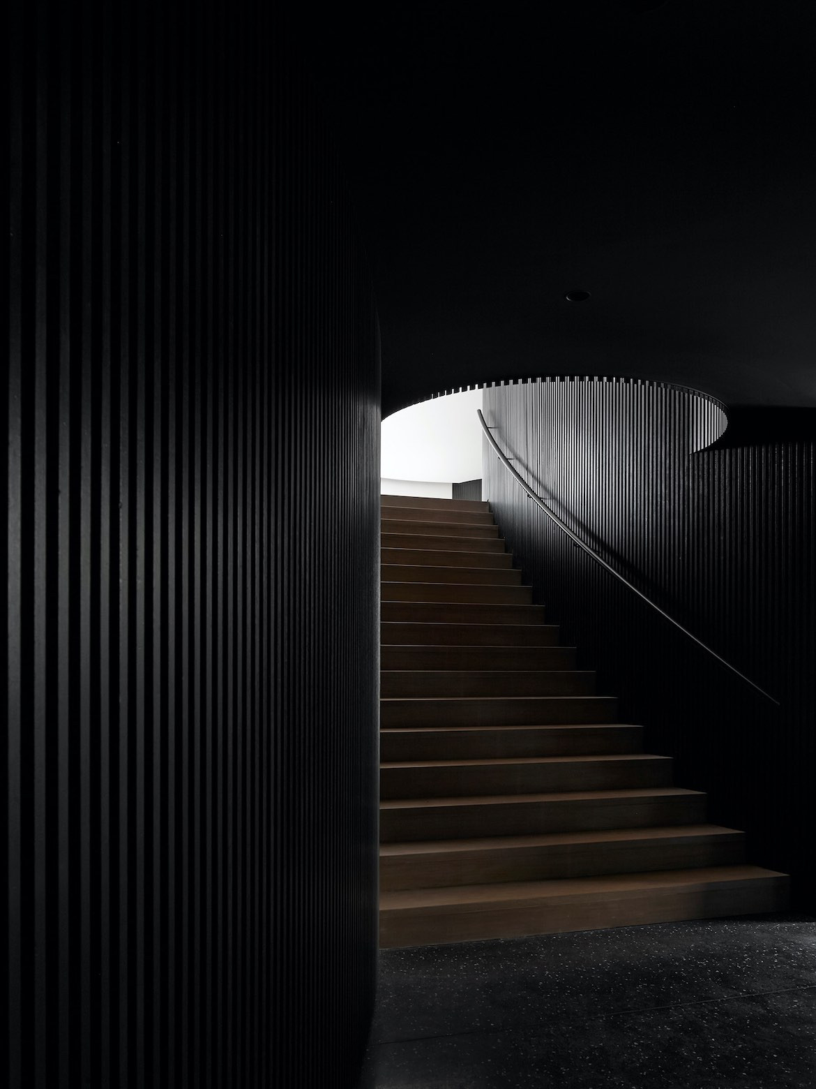 Dark interior cladding and a staircase leading up to the main living area of Portsea House