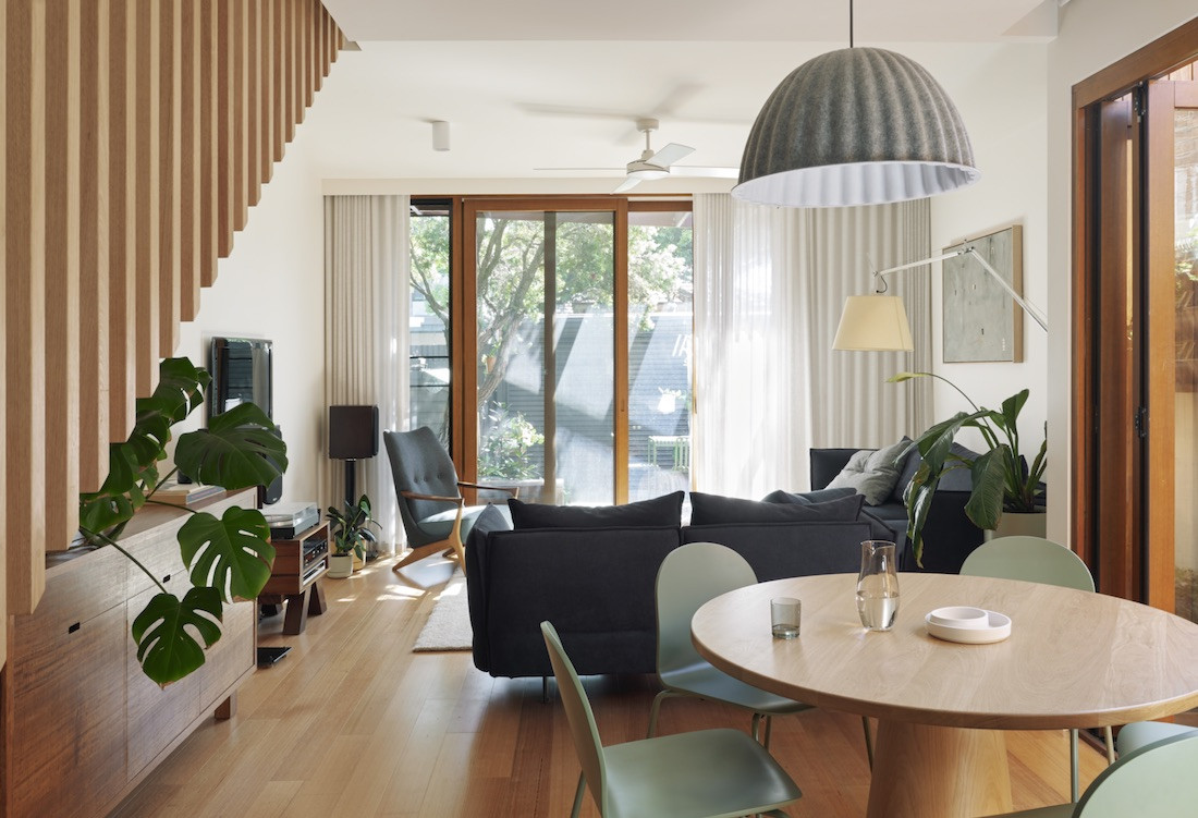 A round dining room table with sage chairs in the foreground and a living room in the background of the Brunswick home.