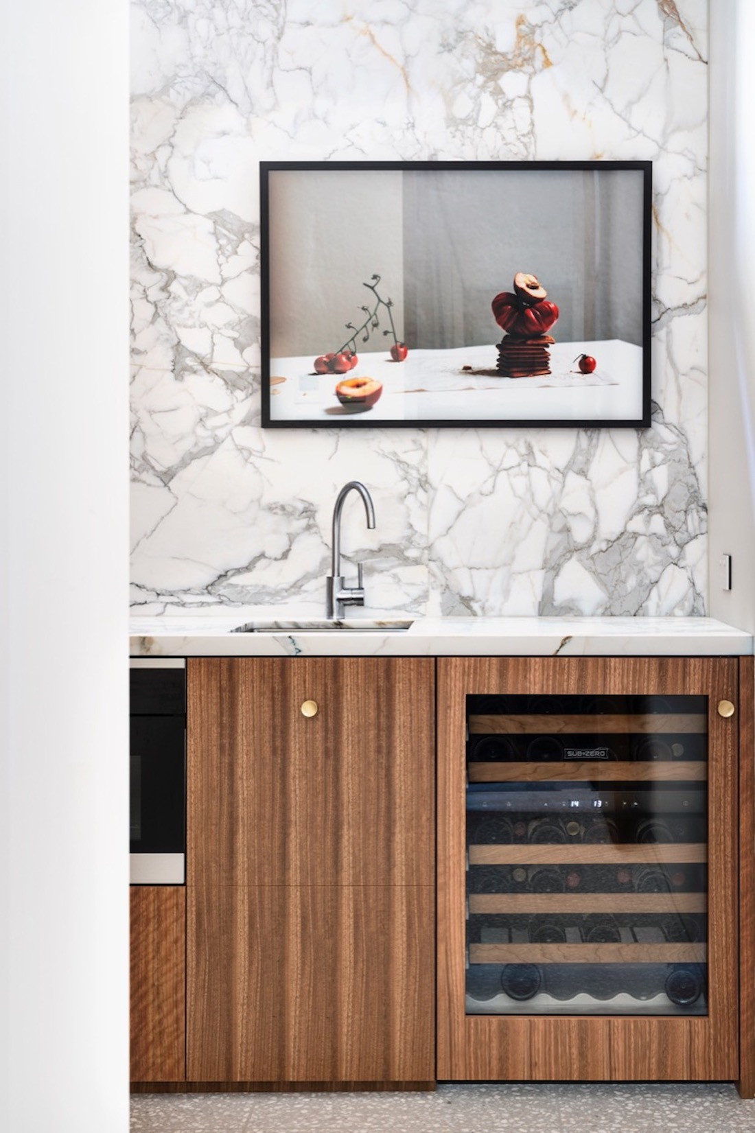 A wine fridge is encased in timber veneer and sitting under an artwork.