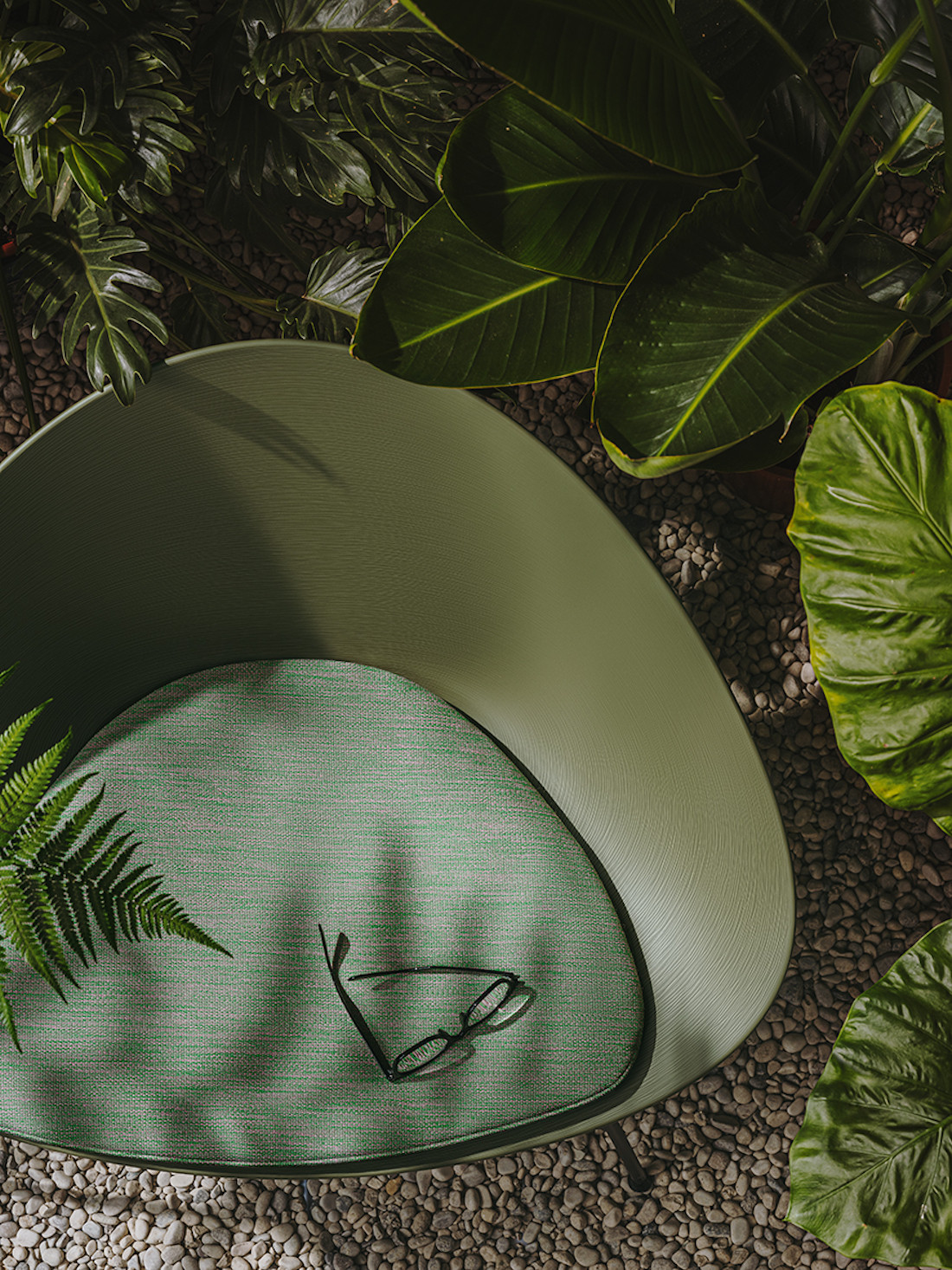 An olive green polypropylene Adell lounge chair by Arper is surrounded by green folliage.