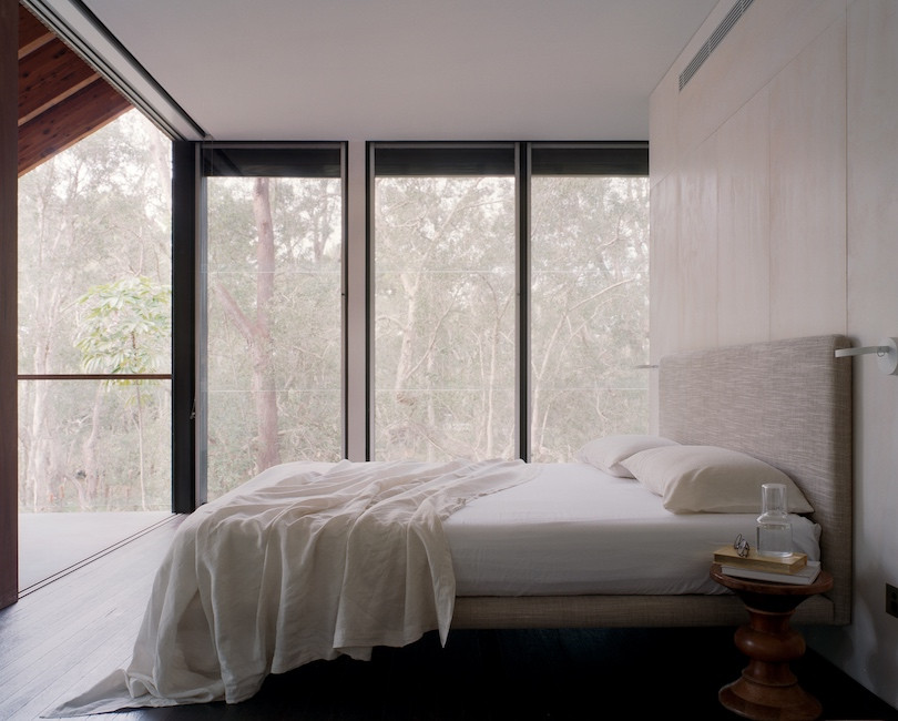 A white and cream bedroom with large windows in Pearl Beach House