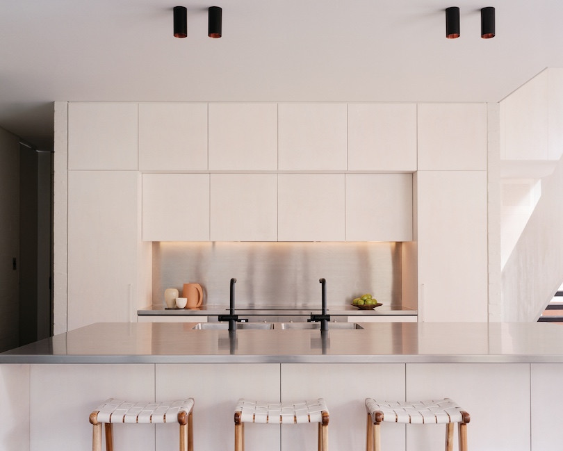 Three wood and white stools line the kitchen island bench in the white kitchen of Pearl Beach House