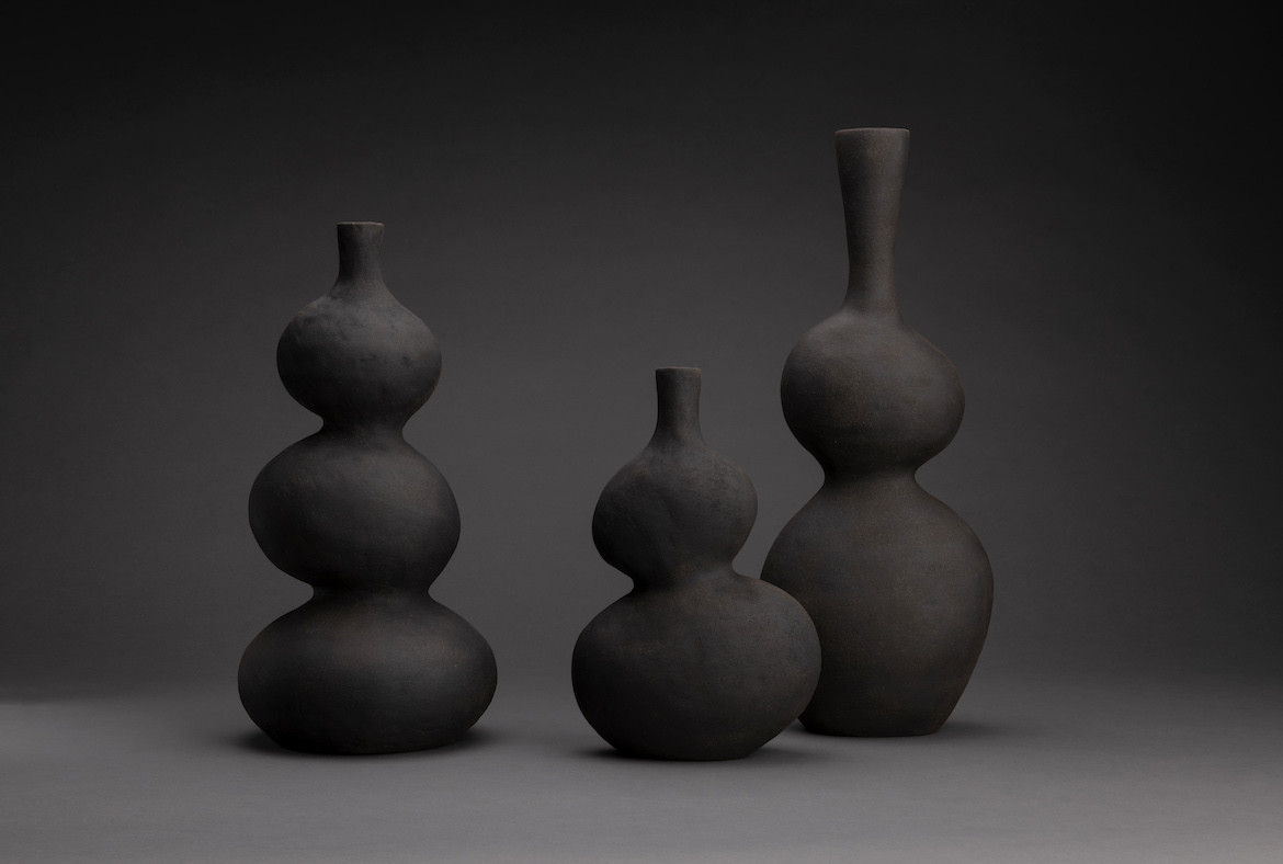 Three of Eloise White's black ceramic vessels on a black background.