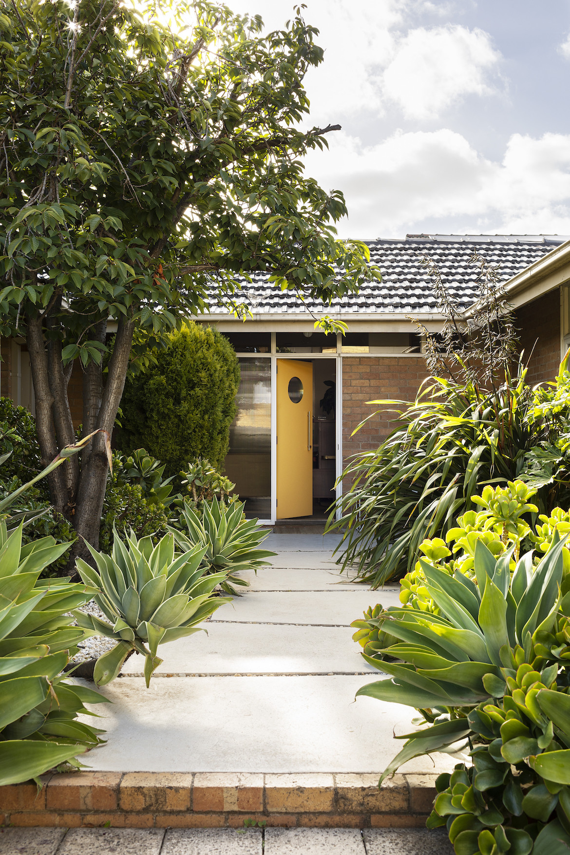 The yellow front door of the brick home stands slightly ajar.