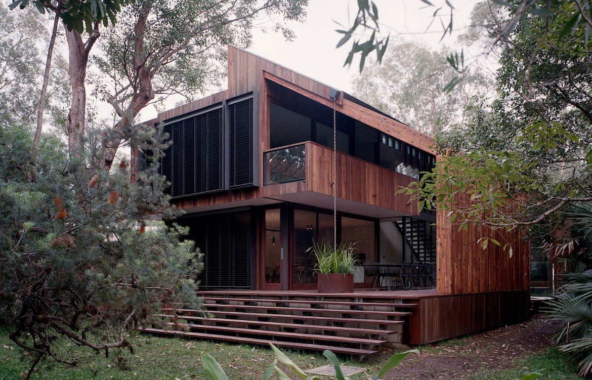 Wooden steps leading up to the rear wood facade and angled roof of Pearl Beach House