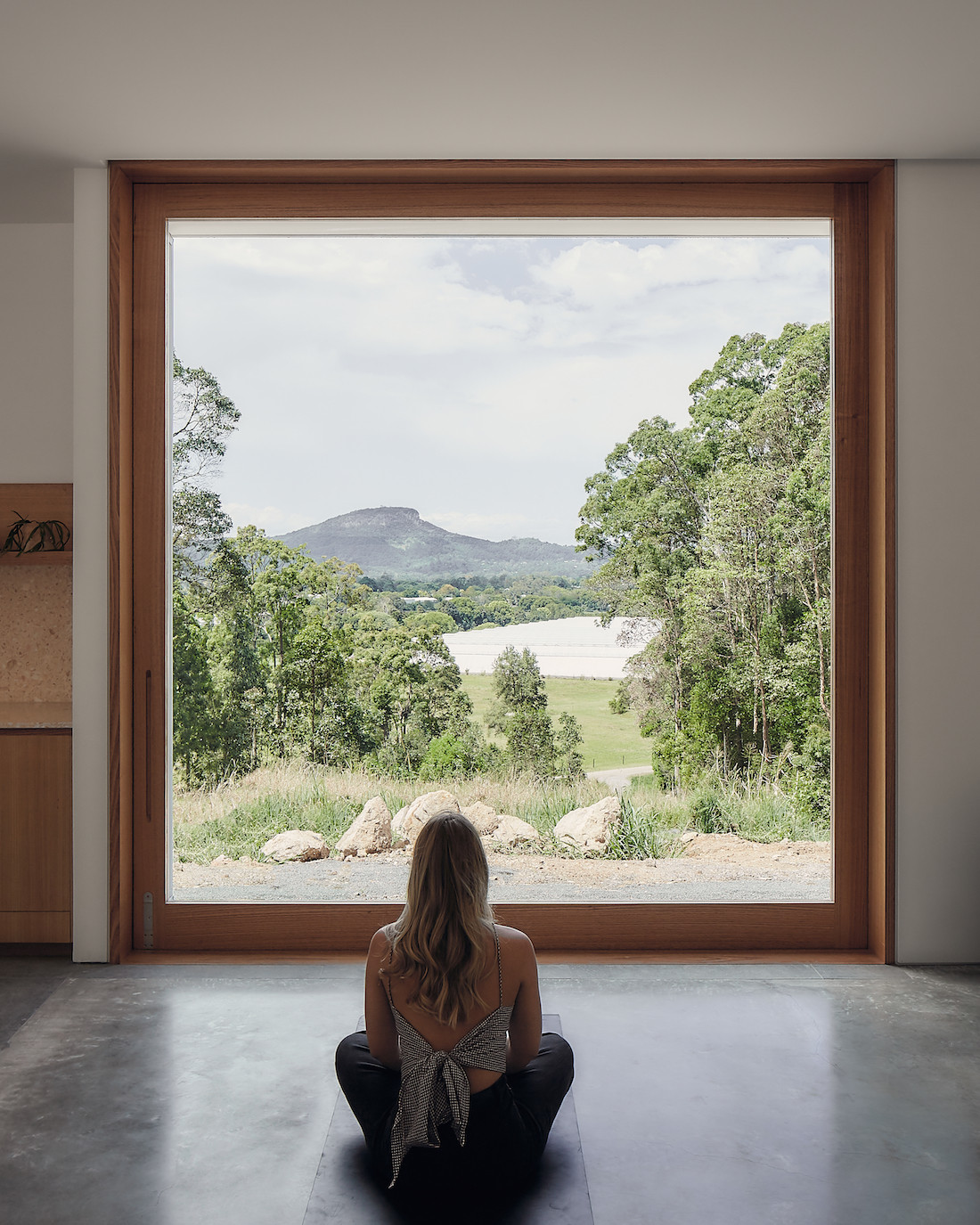 A person sits inside A-CH's Yandina Sunrise home, looking out a large window.