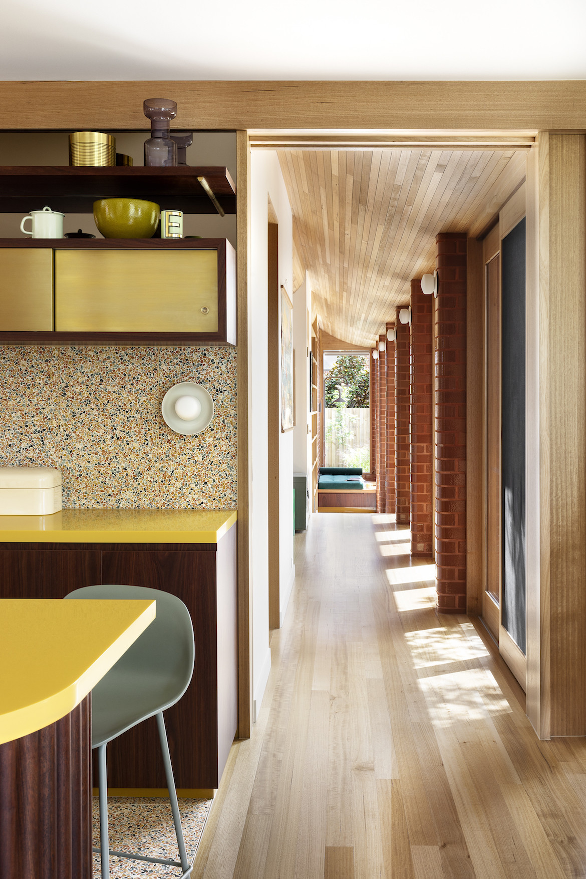 A view down the hallway with a slanted wooden roof and the edge of the kitchen's yellow bench and colourful terrazzo.