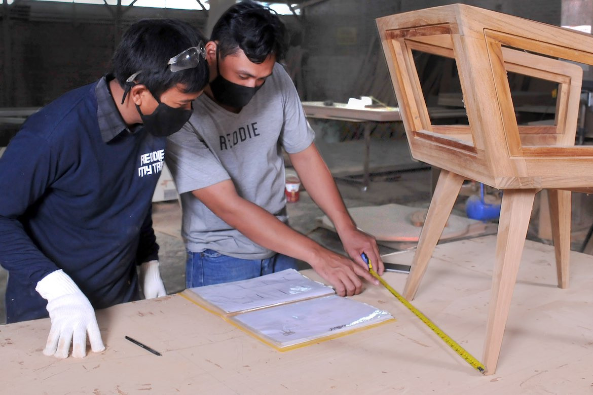 Two men measure the distance between a Reddie chair's legs in the Reddie factoy.