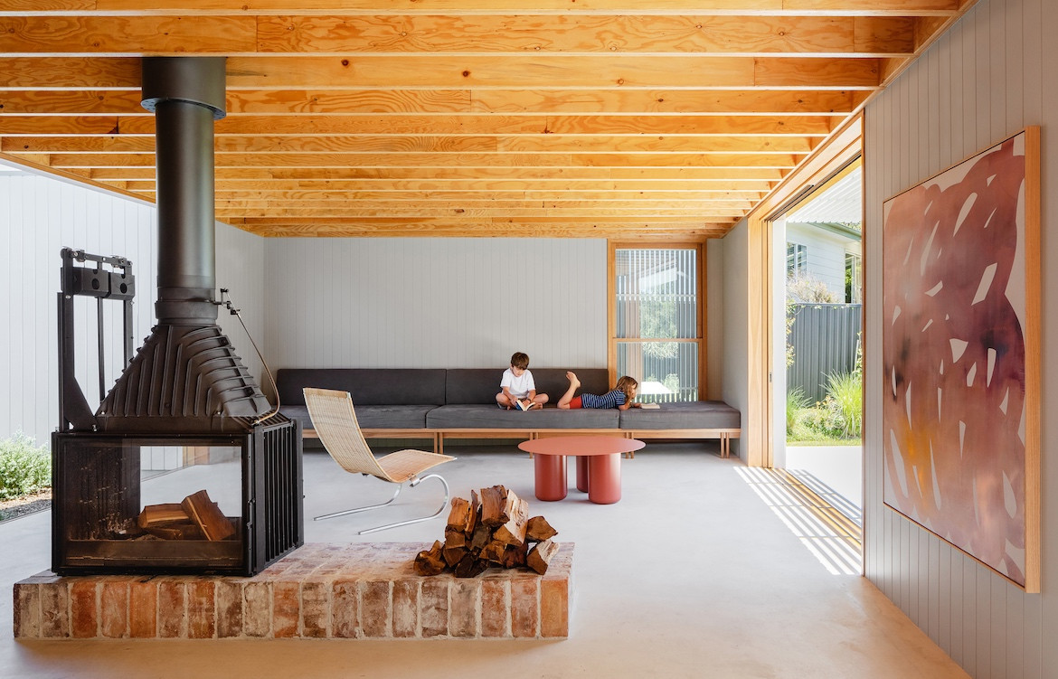 Two kids sit on the couch of the large open-plan living area in Tribe Studio Architect's Bundeena Kit Home.
