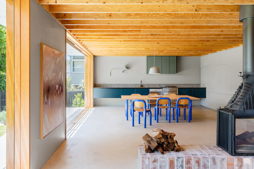 Six blue-framed chairs surround a dining table in the open-plan living room/kitchen of Tribe Studio Architect's Bundeena Kit-Home.