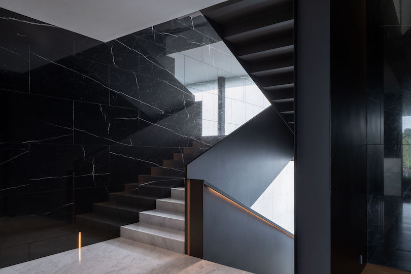 A platform between levels of white marble stairs, with black balustrades and a black shiny marble wall.